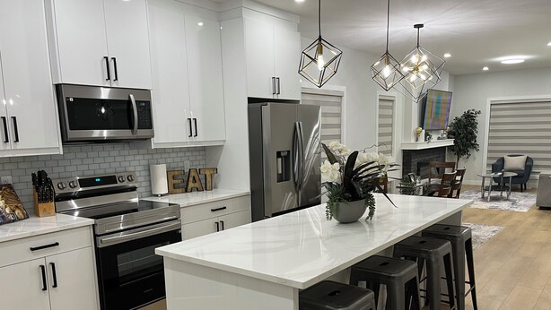 A modern kitchen with white cabinetry, stainless steel appliances, and a central island with bar stools.