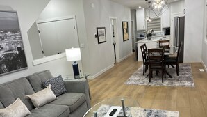 A modern living room with a grey sofa, a glass coffee table, and a dining area with wooden chairs and a rug.
