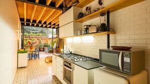 Eine kompakte Küche mit Gasherd, Mikrowelle und kleinem Kühlschrank. Ein Holzboden und der Blick in einen Garten durch eine offene Tür.