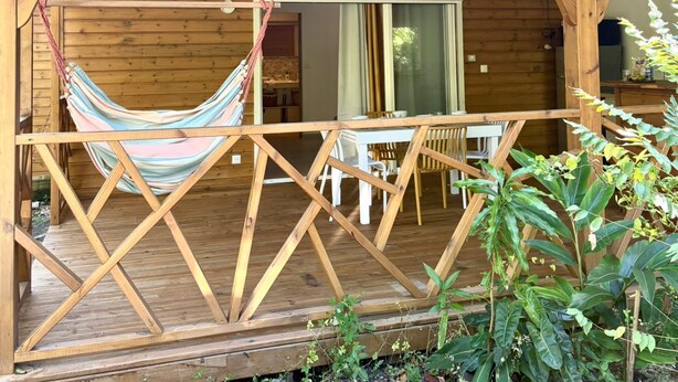 Una cabaña de madera con hamaca, comedor y terraza cubierta.