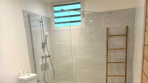 Un baño moderno con cabina de ducha de vidrio, inodoro, un ventanal pequeño y una escalera de madera.