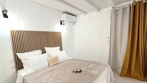 Una cama bien hecha con cabecera, aire acondicionado de pared y una cortina en la ventana.