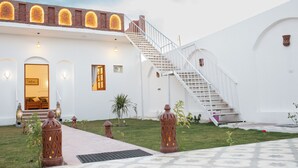 Un edificio blanco con una escalera que lleva a una puerta, rodeado de plantas pequeñas y faroles decorativos.