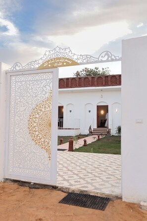 Una entrada con un portón decorativo, un edificio de ladrillo y un camino que lleva a la entrada.