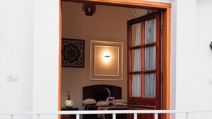 Un balcón con una mesa y sillas de madera, vista hacia un cuarto con cama y lámpara.