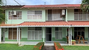 Um edifício de dois andares com telhado de telhas, varanda coberta e caminho de tijolos até a entrada.