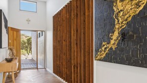 Ein Flur mit einer Wand aus Holzlatten, Holzboden, einem Schreibtisch mit einer Vase und einem großen abstrakten Gemälde.