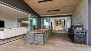Ein zeitgemäßer Wohnbereich mit einer großen Schiebeglaswand, einem weißen Sofa, einem Holztisch und einem eingebauten Grill.