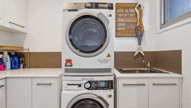 A compact laundry area with a front-loading washing machine, a sink, and a wall-mounted drying rack. - Serena House  Luxury Fingal Retreat with Views (Fingal)