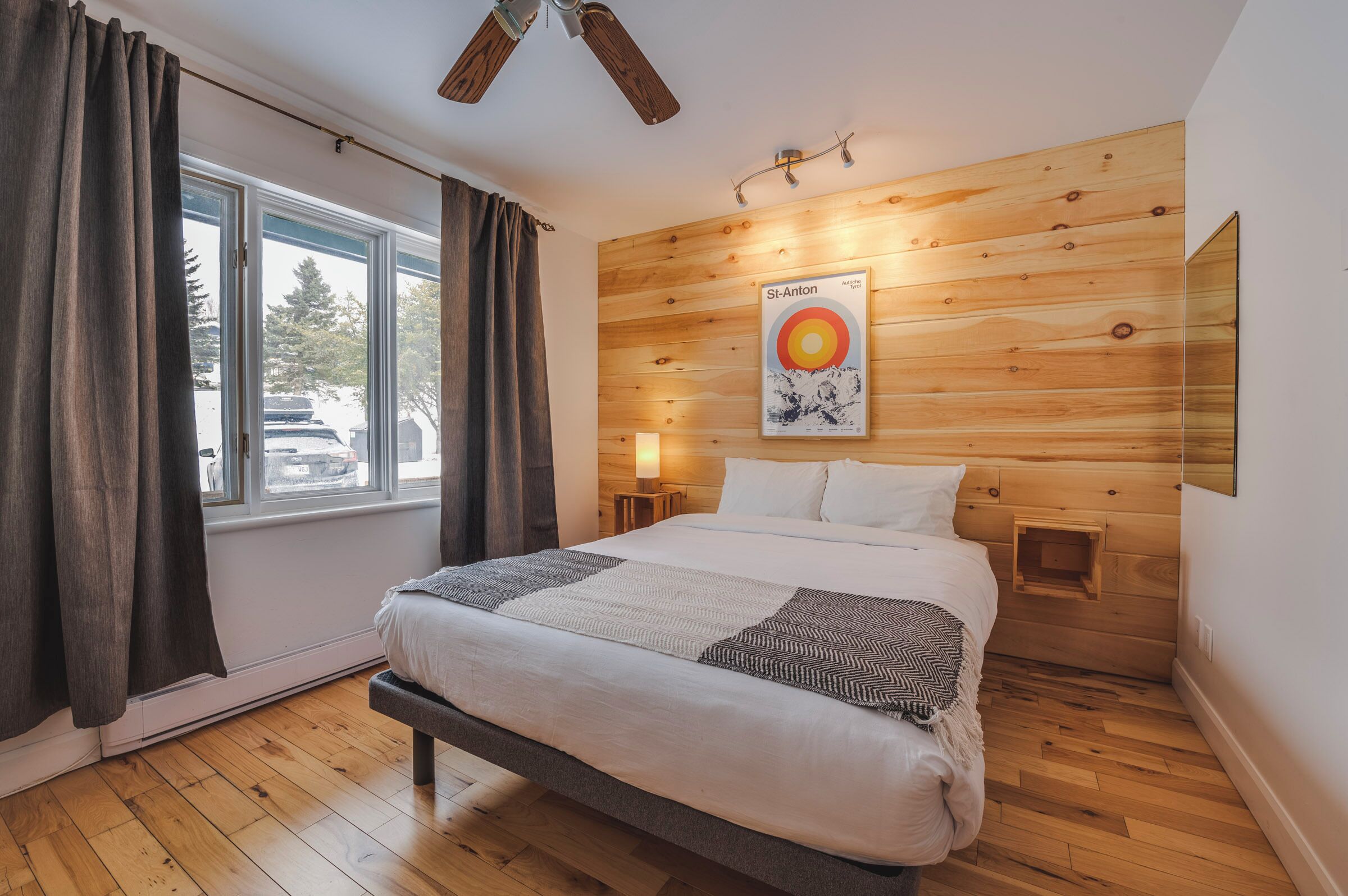 A bedroom with a bed, wooden wall paneling, a poster, and a window with curtains.