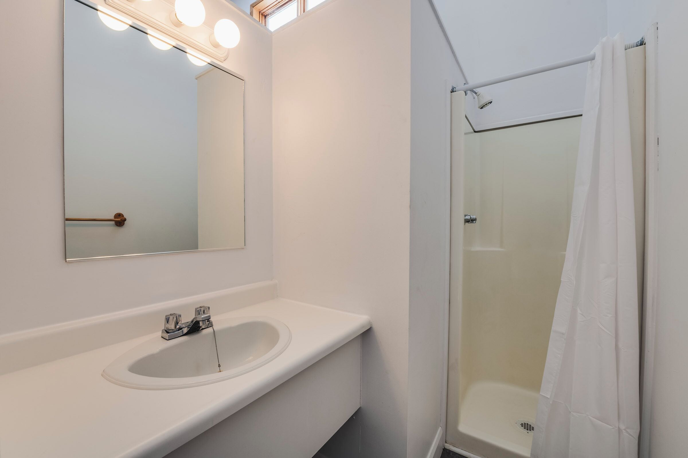 A bathroom with a white sink, mirror, and shower.
