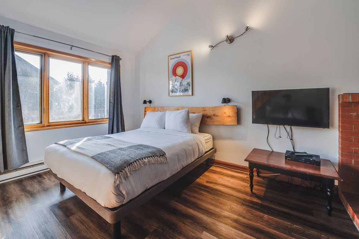 A bedroom with a bed, a TV, a table, and a poster on the wall.