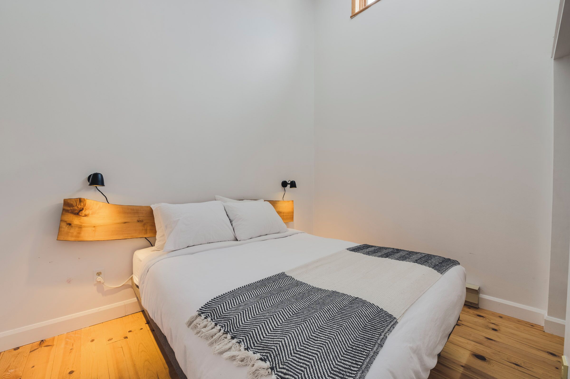 A bedroom with a wooden headboard, white bedding, and a black and white patterned throw blanket.