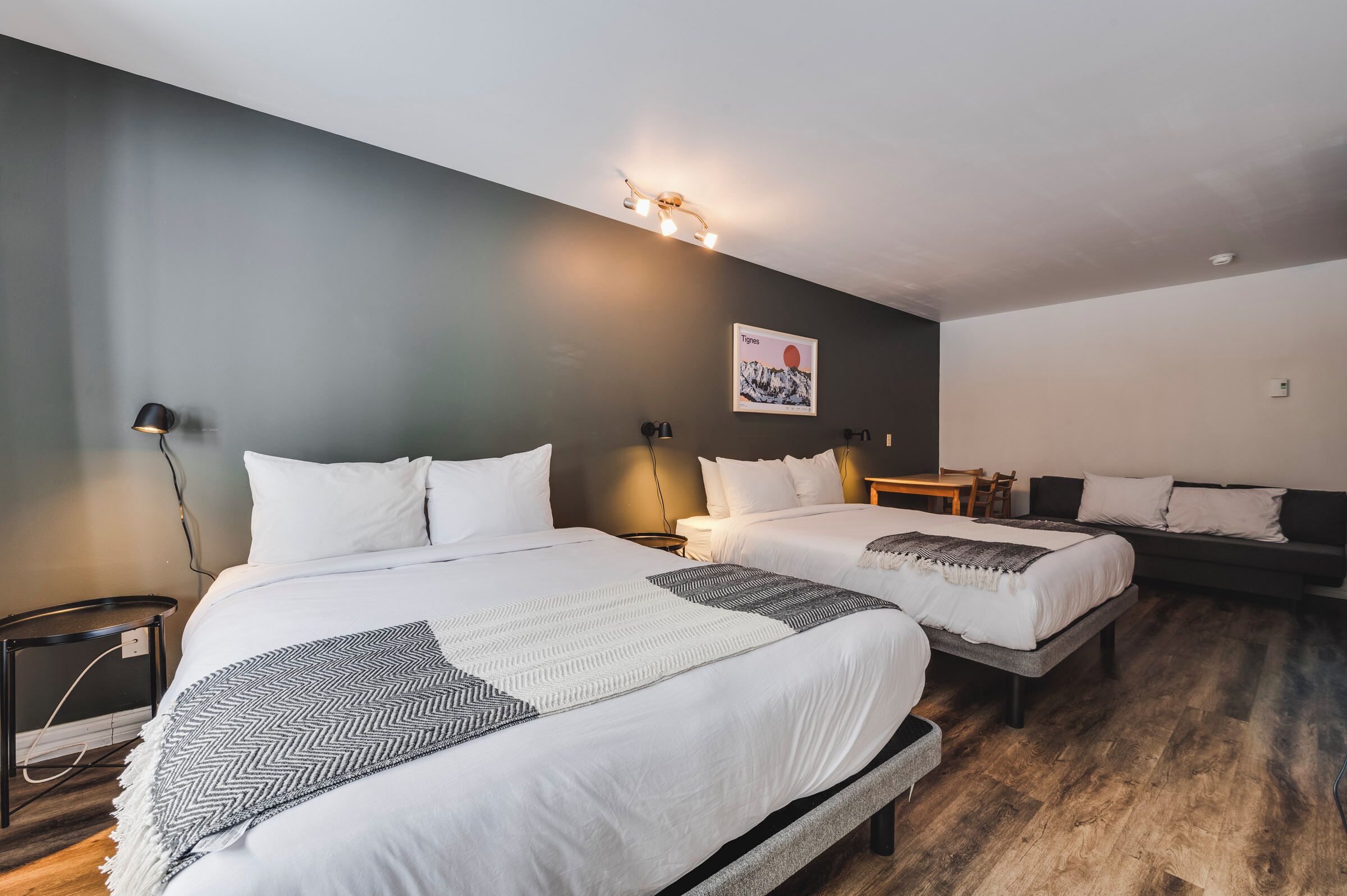 Ein Hotelzimmer mit zwei Betten, einer dunklen Wand, einer Lampe und einem Bergfoto.