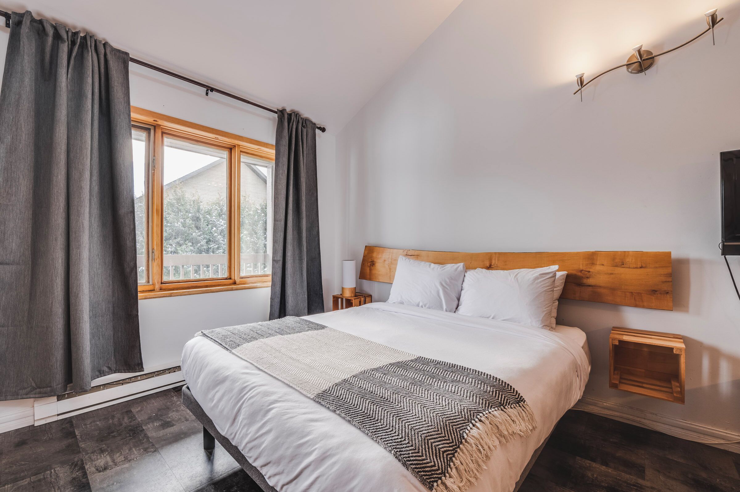 Un dormitorio con una cama grande, una ventana con cortinas, una mesita de noche y una lámpara de pared.