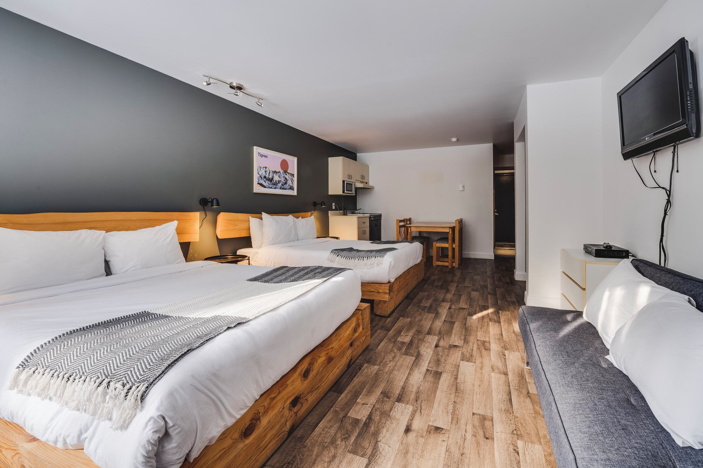 A hotel room with two beds, a TV, a desk, and a kitchenette.