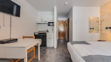 Una habitación de hotel compacta con cama, escritorio, televisor, kitchenette y una pared de acento de madera.