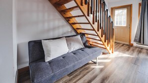 Ein modernes Wohnzimmer mit einem grauen Sofa, einer Holztreppe und einer Tür mit Fenster.