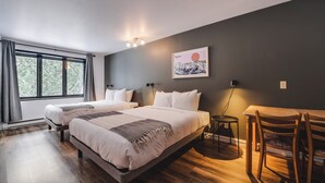 Ein modernes Hotelzimmer mit zwei Betten, einem Esstisch und Blick auf Bäume durch große Fenster.