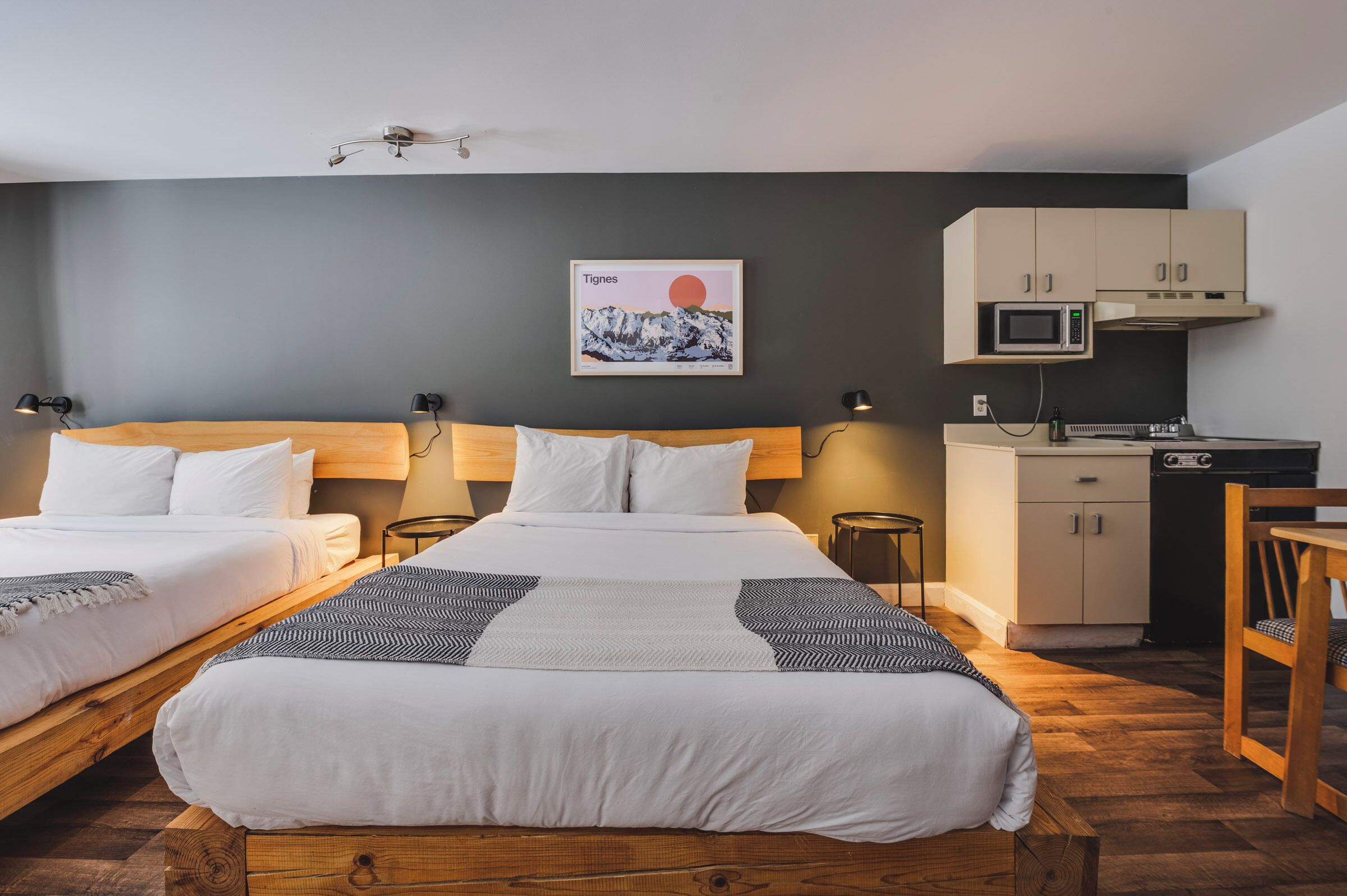 A hotel room with two beds, a kitchenette, and a wall-mounted artwork.