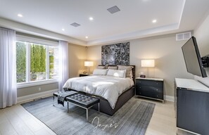 Une chambre à coucher moderne avec un grand lit, des lampes de chevet, un banc, une commode et une grande fenêtre avec des rideaux.