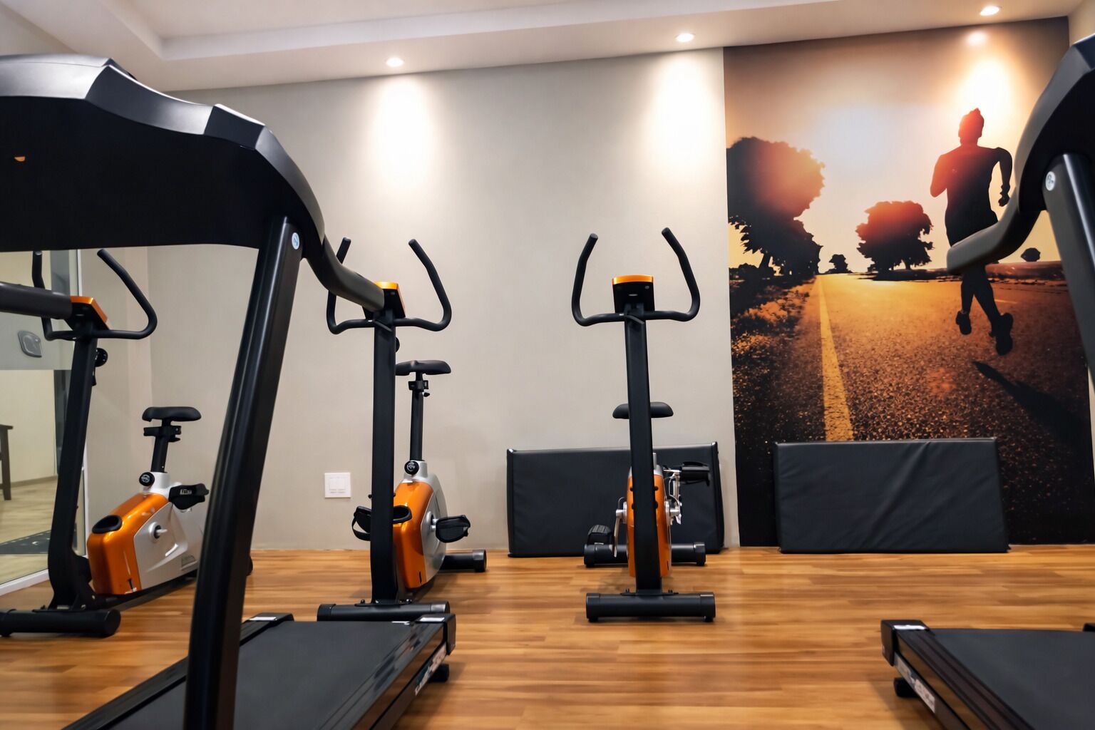 Un gimnasio con cintas de correr, bicicletas estáticas y un espejo grande.