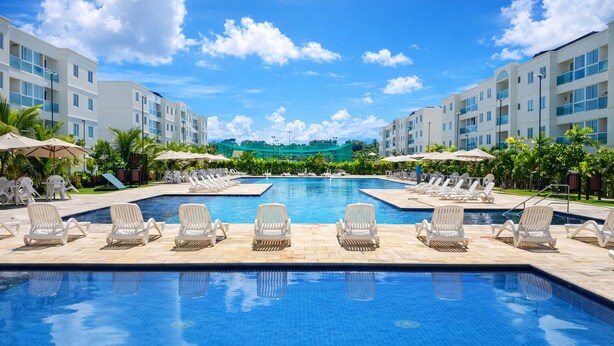 A swimming pool with lounge chairs and umbrellas, surrounded by buildings. - Apto Porto de Galinhas (Ipojuca)