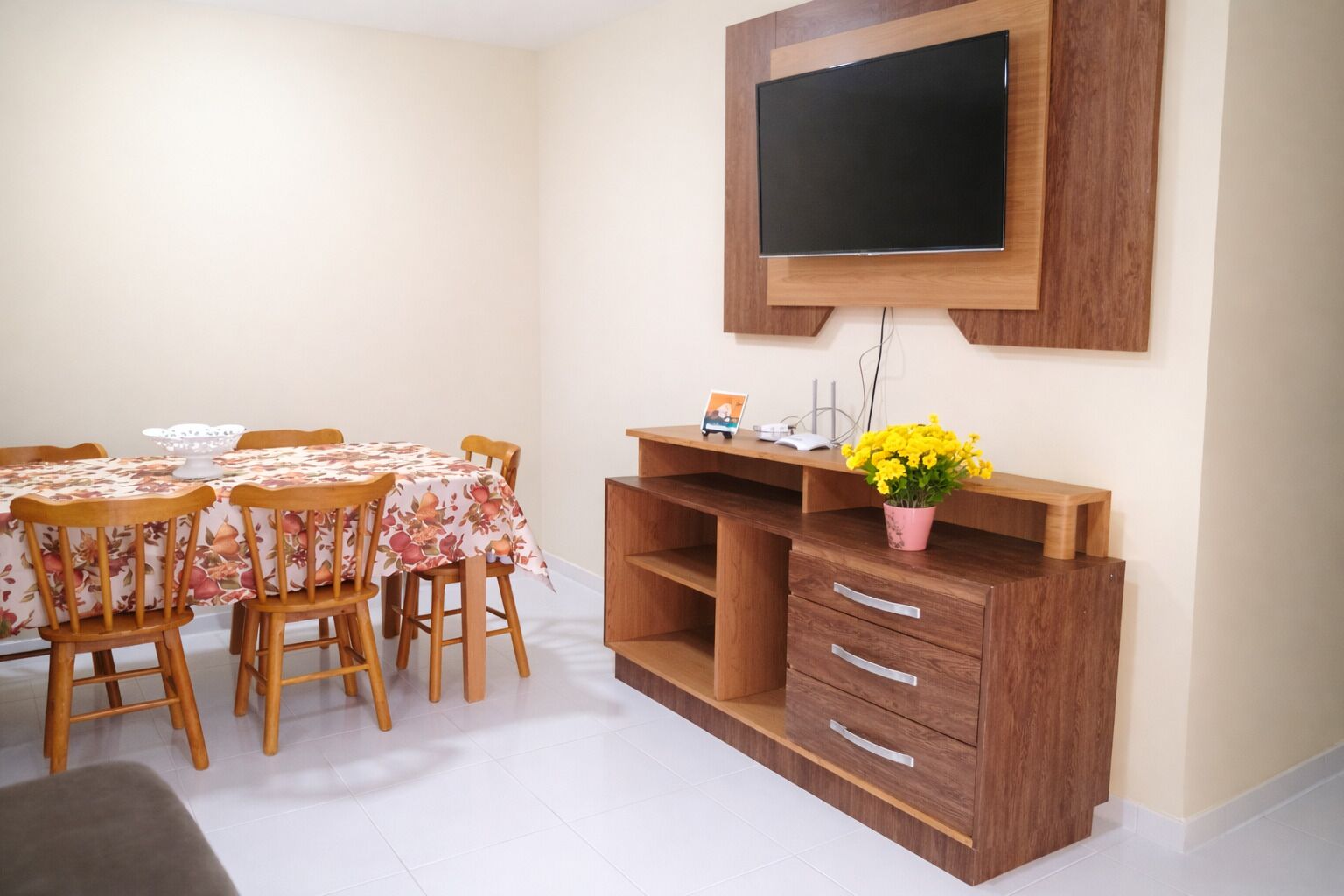 A dining area with a table set for four, a wooden cabinet with drawers, and a mounted television.