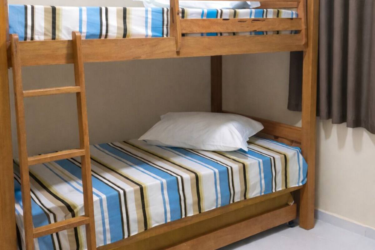 A bunk bed with striped bedding, a wooden ladder, and a woven mat on the floor.