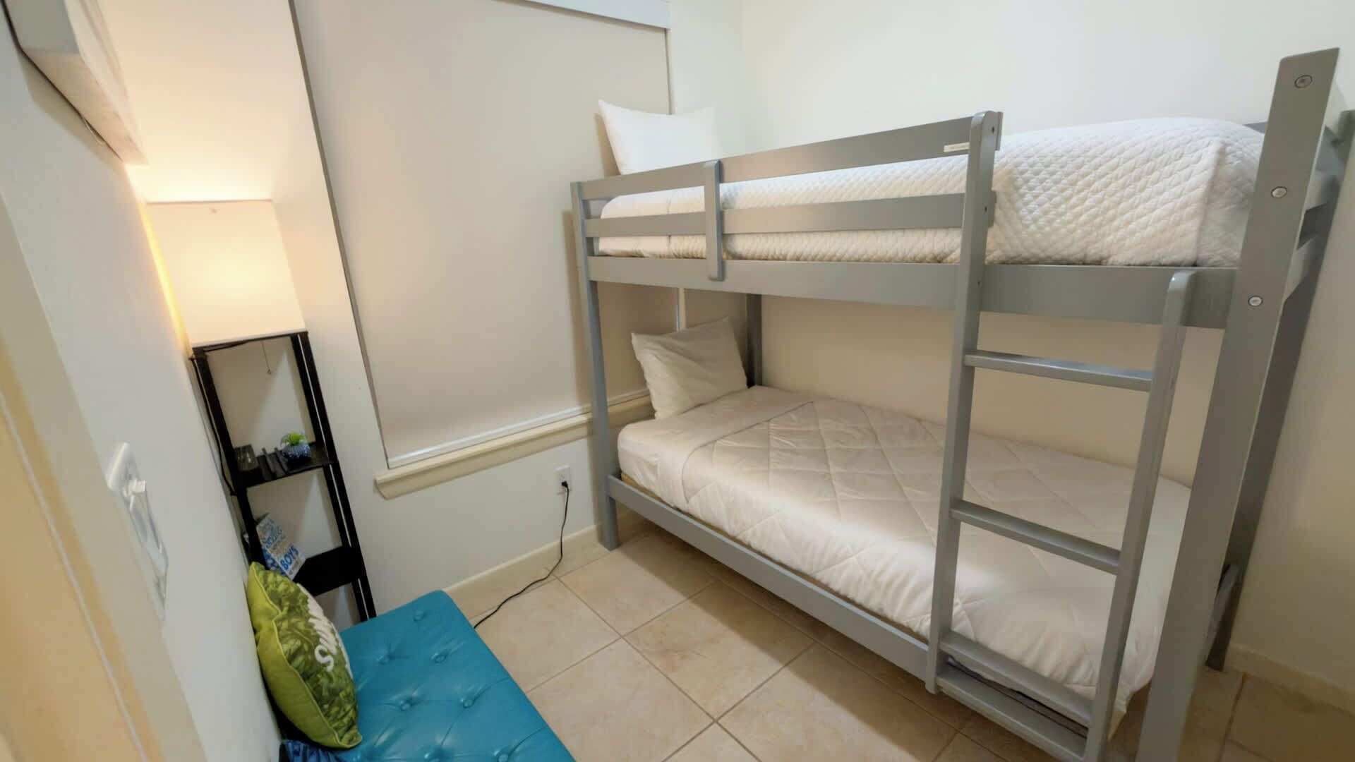 Habitación con literas, un banco azul y una estantería con artículos de aseo.