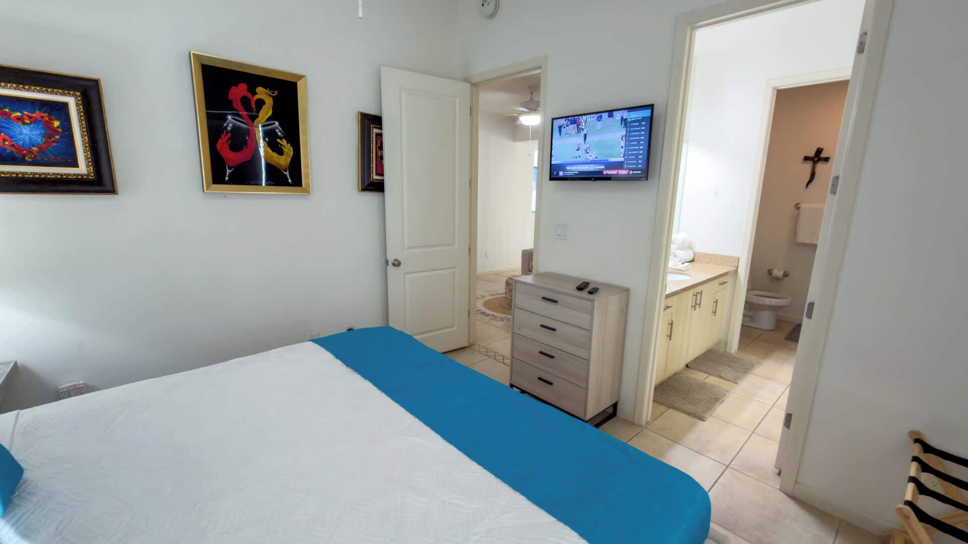 Ein Schlafzimmer mit einem Bett, einem Schminktisch, einem Fernseher und einer Tür zu einem Badezimmer.