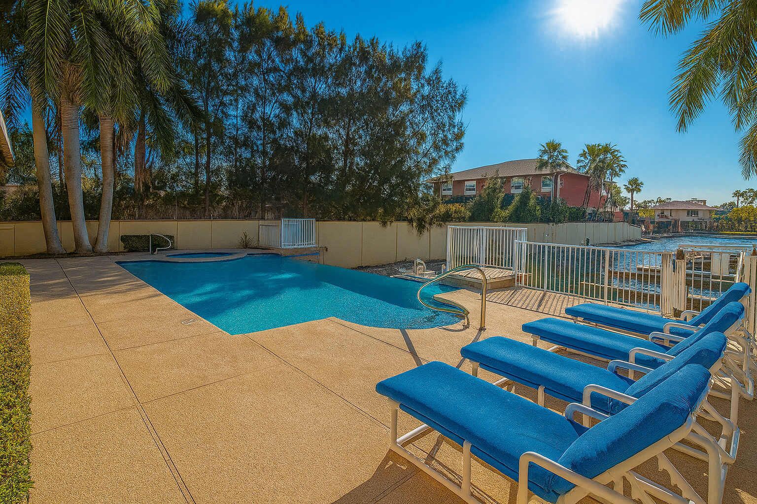 A swimming pool with blue water, surrounded by a tiled deck and blue lounge chairs.