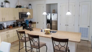 Een moderne keuken met een centraal eiland, barkrukken, roestvrijstalen apparatuur en hanglampen.
