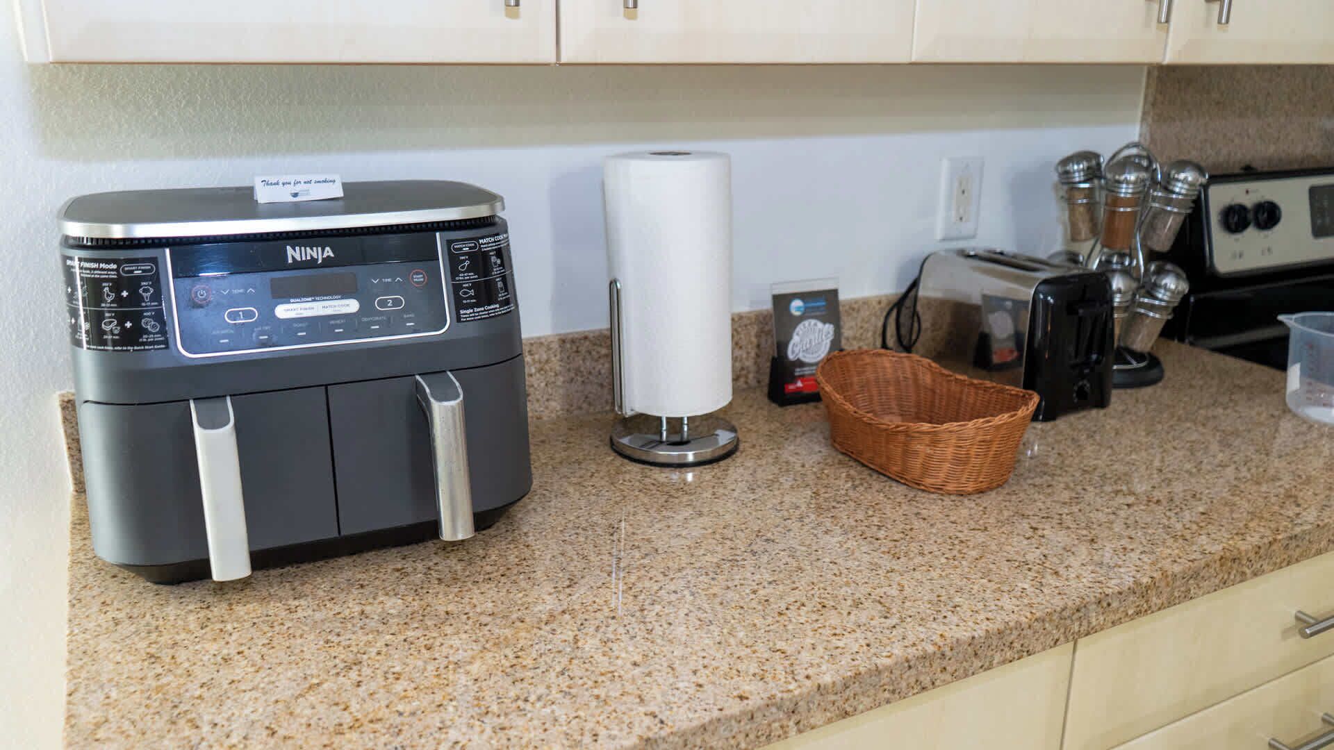 A kitchen with a Ninja air fryer, a paper towel holder, a basket, a toaster, and a coffee maker.