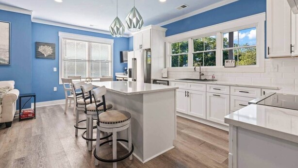 Una cocina moderna con armarios blancos, una isla central con taburetes y un amplio ventanal que ofrece luz natural.