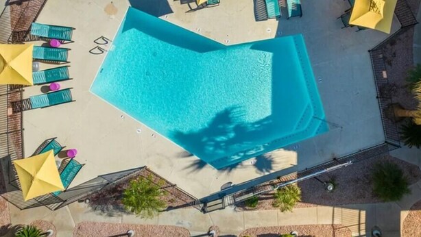 An aerial view of a swimming pool with sun loungers and umbrellas, surrounded by a paved deck and palm trees. - Cozy Stay 8mins to Old Town Scottsdale (Scottsdale)
