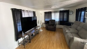 Ein modernes Wohnzimmer mit Flachbildfernseher, Ledersofa, Relaxsessel und Standventilator.