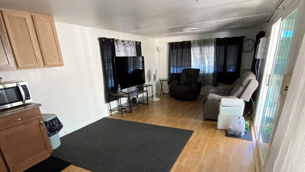 Ein Wohnzimmer mit Deckenventilator, einem Flachbildfernseher, einer Couch und einem Essbereich mit einer Mikrowelle.