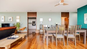 A spacious living room with a wooden coffee table, a TV, and a bookshelf. There is a dining area with a table and chairs, and a kitchen in the background. - Casa Keam is a peaceful private retreat set in the hills of Santana (Santana)