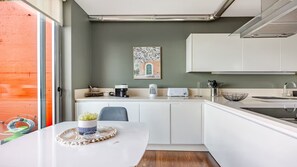 Ett modernt kök med vita skåp, ett matbord med en bordsduk, en kaffebryggare, en brödrost och en diskho med en botten av rostfritt stål.