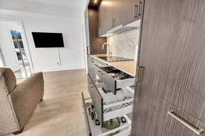 A modern kitchen with a built-in stove, a sink, and a marble backsplash. There is a flat-screen TV mounted on the wall and a sofa in the adjacent living area. - Luxury 2BR/2BA at The Well | Pool, Gym & Downtown Views (Toronto)