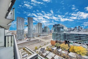 A high-rise building with a modern glass facade, a train track running parallel to the building, and a mix of residential and commercial structures in the background. - Luxury 2BR/2BA at The Well | Pool, Gym & Downtown Views (Toronto)