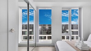 Une chambre moderne avec un grand lit, une vue sur un immeuble à travers de grandes fenêtres du sol au plafond et une porte-fenêtre coulissante donnant sur un espace extérieur.
