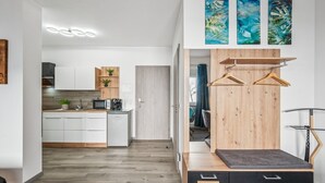 Een moderne keuken met witte kastjes, een magnetron en een koffieapparaat. Er is een houten kast met een plantenplank en een houten bank met een zwart kussen.