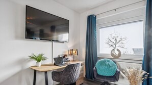 Een moderne kamer met een bureau, stoel, televisie en een raam met gordijnen.