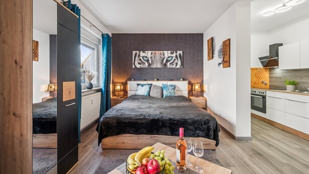Een moderne slaapkamer met een groot bed, nachtlampjes, uitzicht op de stad en een kitchenette.