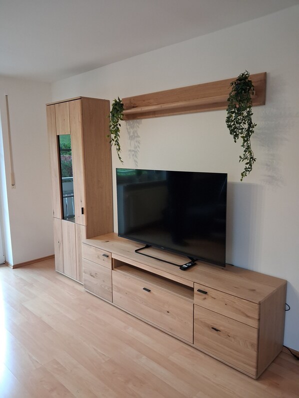 Un mueble de madera con televisor de pantalla plana, cajones y plantas colgantes.