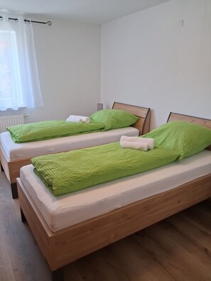 A room with two wooden beds, each with green bedding and white towels. - Eva Apartment with a Balcony on the Edge of the Forest (Woringen)