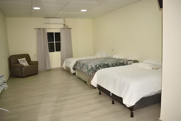 A bedroom with a single sofa, two beds, a window with curtains, and a ceiling vent.