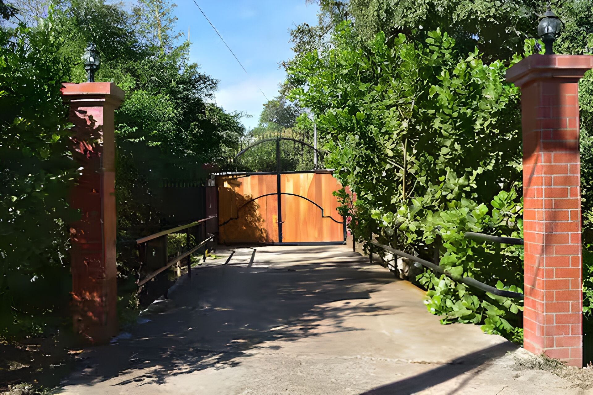A gated entrance with a wooden gate, surrounded by lush greenery and a brick wall.